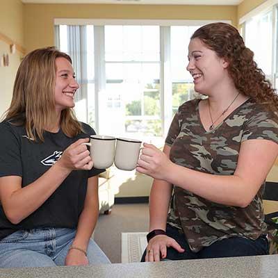 two students sit at a counter in their dorm and clink mugs