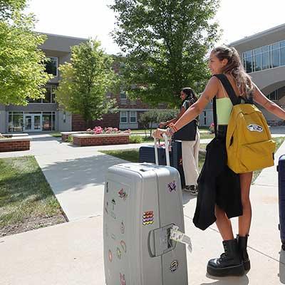 a student rolls a suitcase outside her dorm